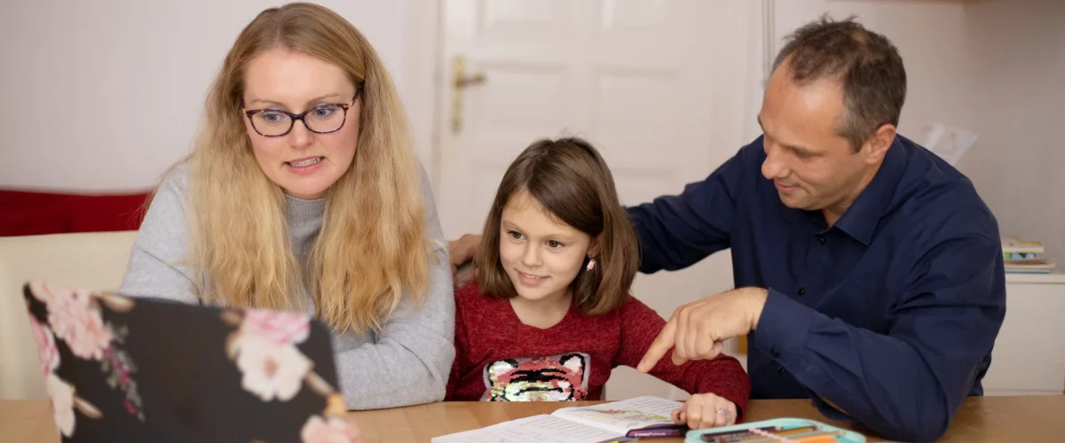 Familienbeihilfe Voraussetzungen – Familie sitzt am Tisch und bespricht die Familienbeihilfe Voraussetzungen in Österreich, im Hintergrund ein Laptop mit Finanzamt-Webseite.