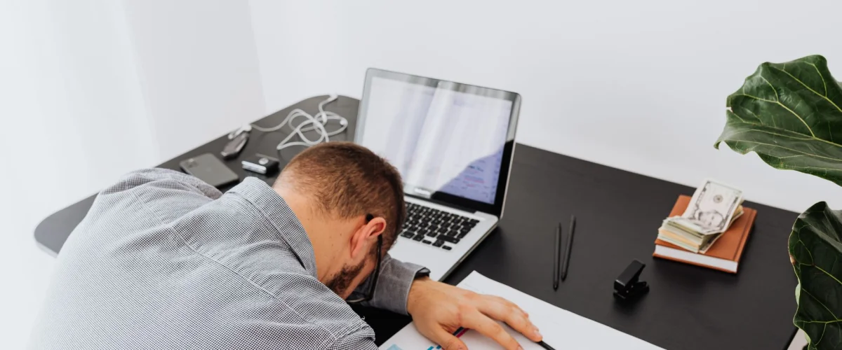 Burnout-Prävention seriös erkennen – Eine Person sitzt nachdenklich an einem Schreibtisch und überlegt, wie sich Burnout-Prävention seriös erkennen lässt.