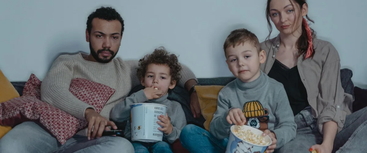 Familienfilme kündigen – Eine Familie sitzt vor dem Fernseher und ein Erwachsener hält ein Tablet mit Kündigungs-Optionen.