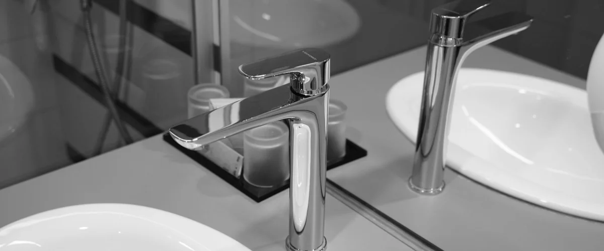 Sanitärbetrieb beauftragen: Ein Fachmann prüft Rohrleitungen in einem Badezimmer